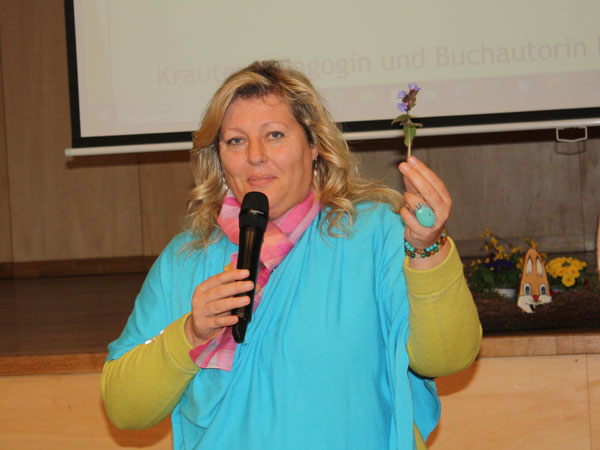 Eunike Grahofer hält eine Pflanze des Lungenkrauts in die Höhe und in der Anderen Hand das Mikrofon bei ihrem Vortrag