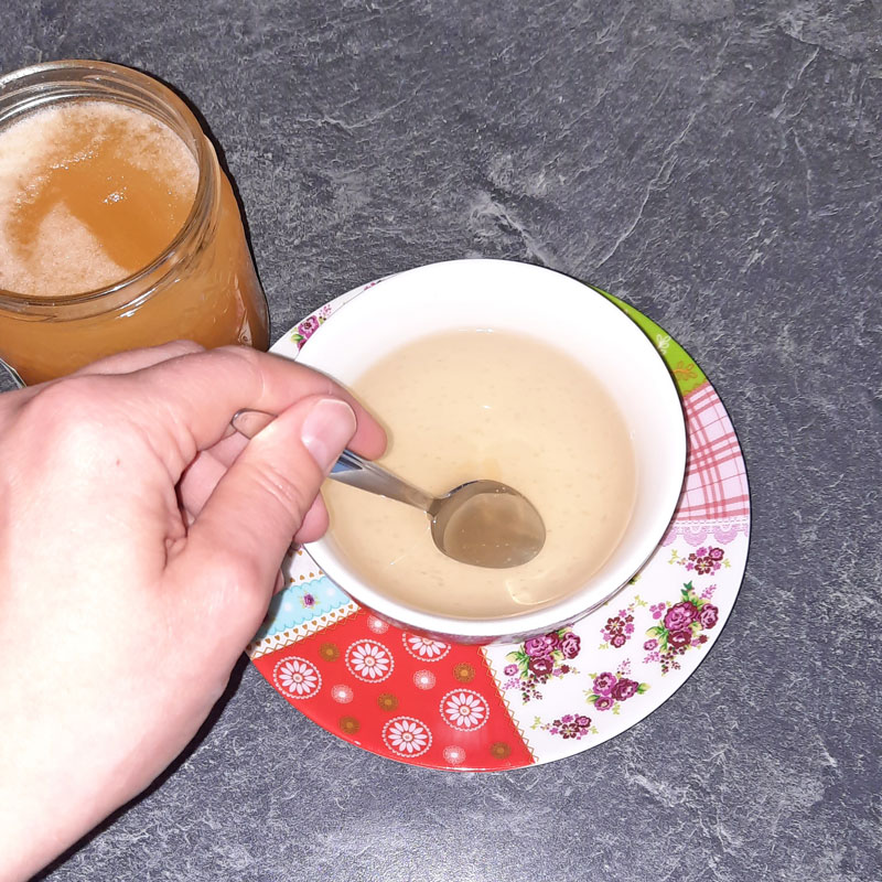 Teetasse mit Holunderrinden-Tee. Es wird gerade ein Teelöffel Honig eingerührt.